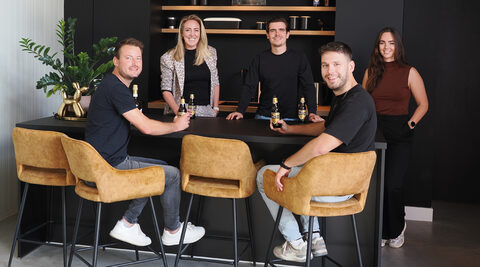Het team van Amigo rond de zwarte bar in hun kantoor, op gele barkrukken en met een flesje bier in de hand.