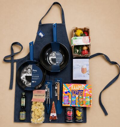 Kerstpakket voor Smits Vastgoedzorg, uitgestald op een schort van gerecyclede jeans: twee pannen van Hugo Kennis, een doosje verse groenten, tagliatelle, olijfolie, een bierglas-cadeau, een kleurrijk Kaapse Kwartet en twee blikken soep.