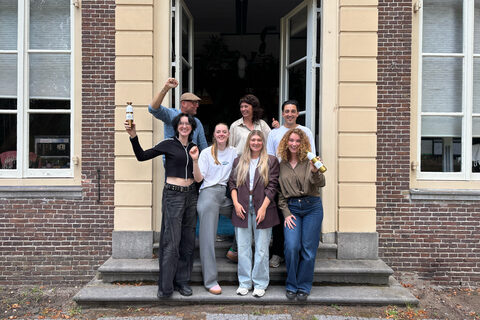 Het team van Greenmotion op de bordestrap voor het kantoor, juichend, twee van hen met een fles in de hand.