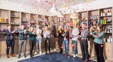 Het team van IGO Promo schiet confettikanonnen af in de showroom, voor wandkasten vol drinkflessen, mokken en thermosbekers.