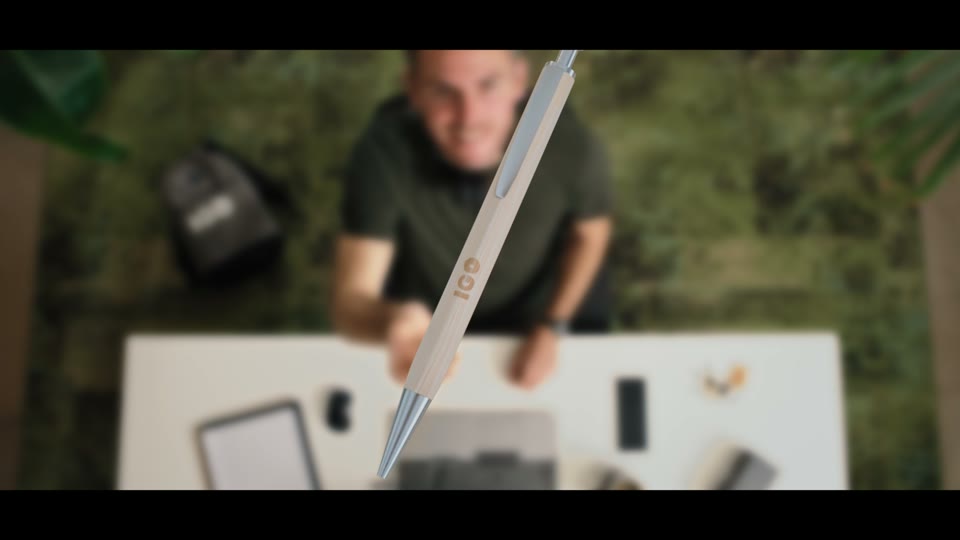 Stilstaand beeld uit de bedrijfsvideo van IGO Promo: een houten pen met IGO-logo valt boven een bureau waaraan een man zit te werken.