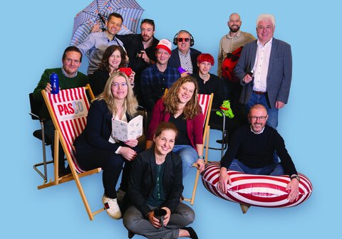 Het team van Pasco Gifts op een lichtblauwe achtergrond, met een gestreepte strandstoel, een zwemband, een paraplu en ander eigen promotiemateriaal in de hand.