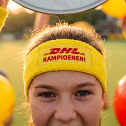 Een speelster met een gele DHL-hoofdband met de tekst 'DHL Kampioenen!' achter een kampioensschaal.