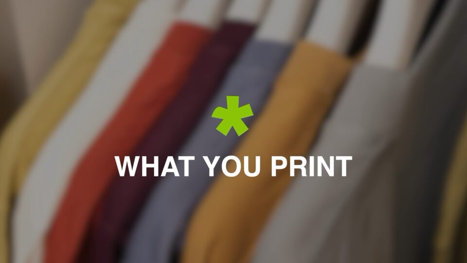 Stilstaand beeld uit de bedrijfsvideo van Wazabi: een rek met gekleurde overhemden, met daarover het groene Wazabi-asterisk en de tekst “WHAT YOU PRINT”.